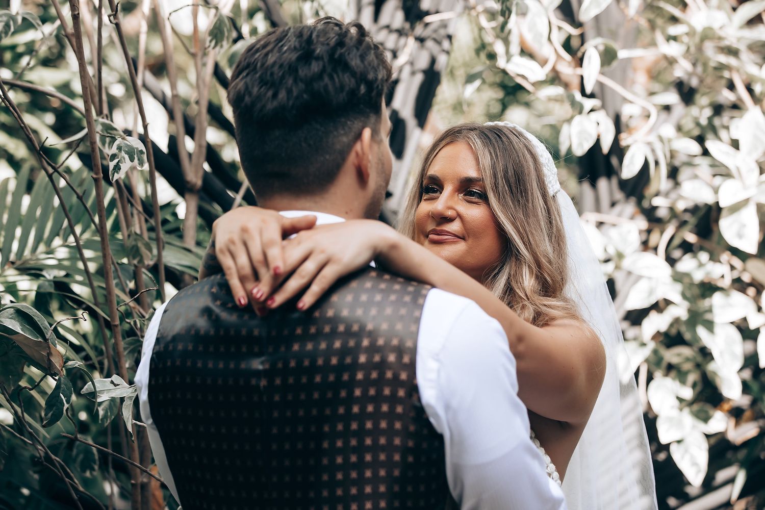A couple shares an intimate moment in a garden setting surrounded by white floral blooms.