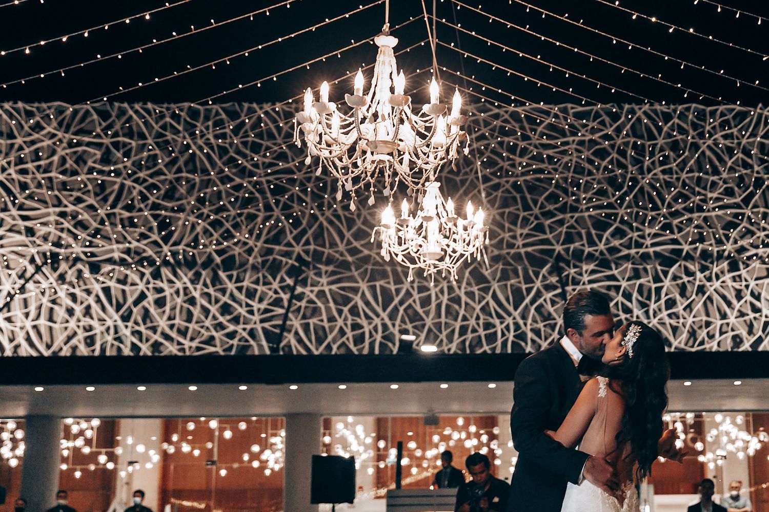 Wedding reception venue decorated with crystal chandeliers and twinkling string lights overhead.