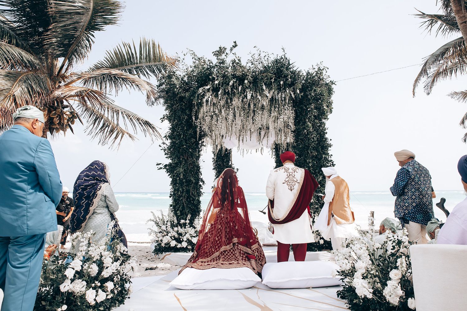 Elegant beach wedding setup with white decor, palm trees, and ocean views in the background.