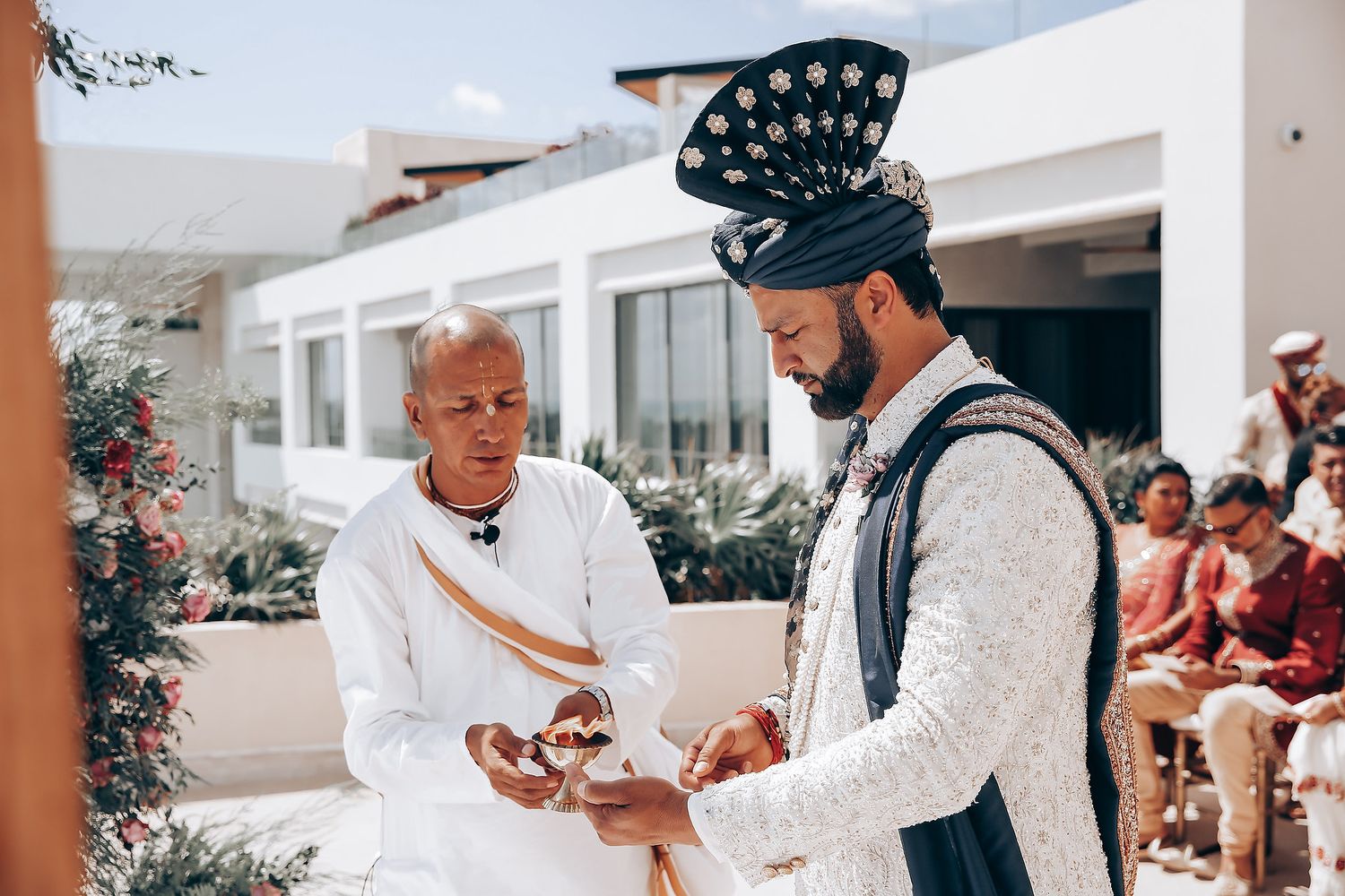 Two people in traditional attire having an animated conversation at an outdoor venue with white buildings in background.