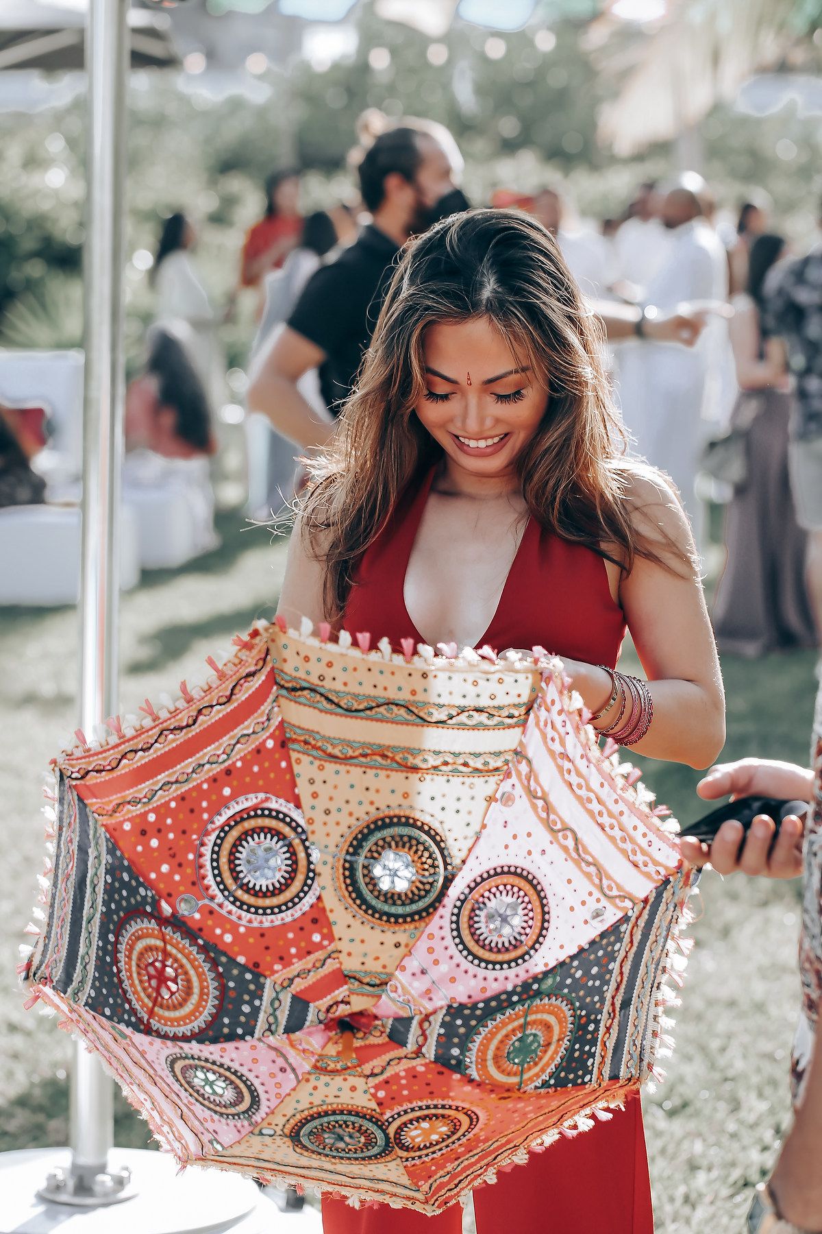 Woman in red dress admiring colorful patterned parasol with intricate circular designs at outdoor event.