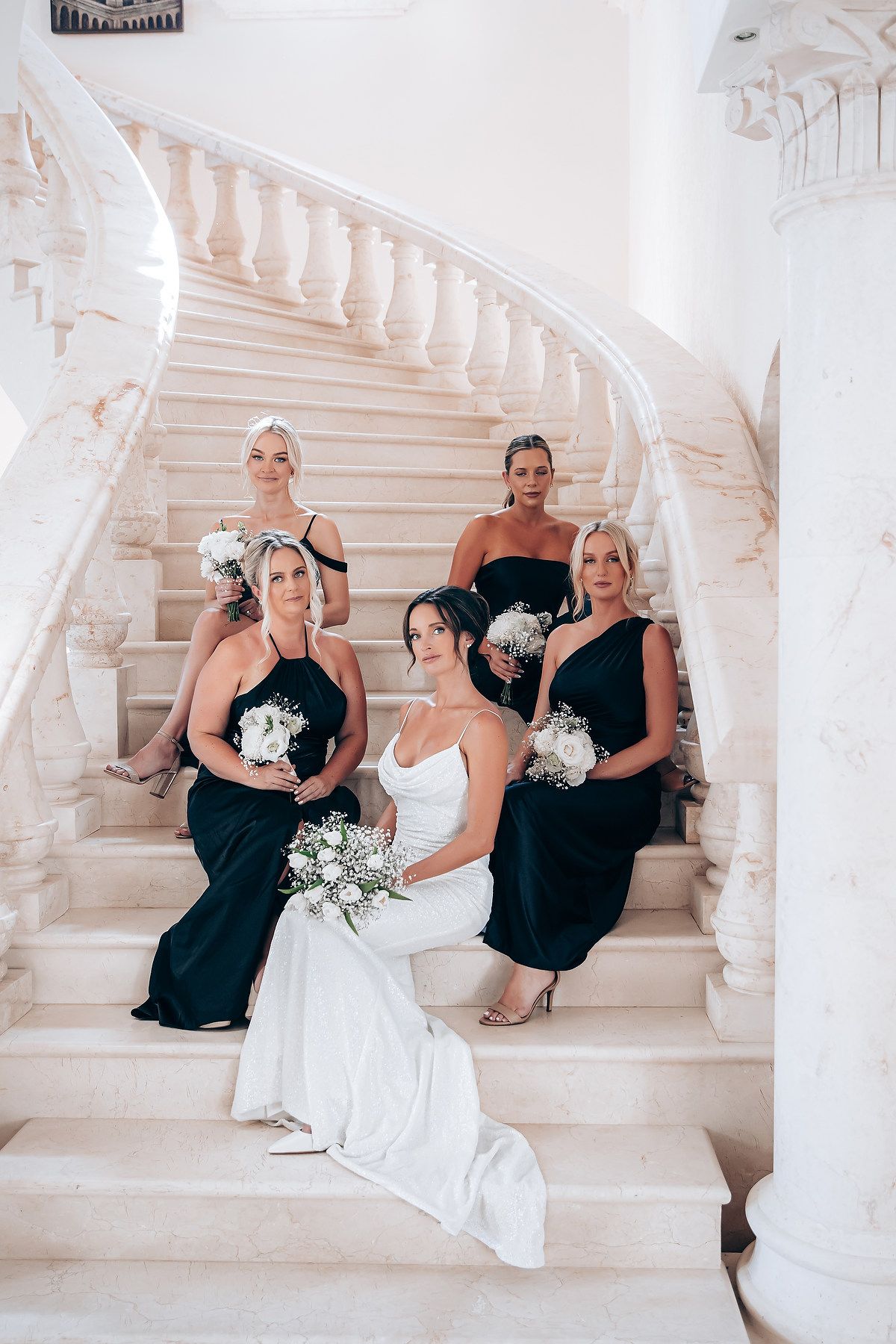 Wedding party poses on elegant white marble staircase wearing black and white formal attire.