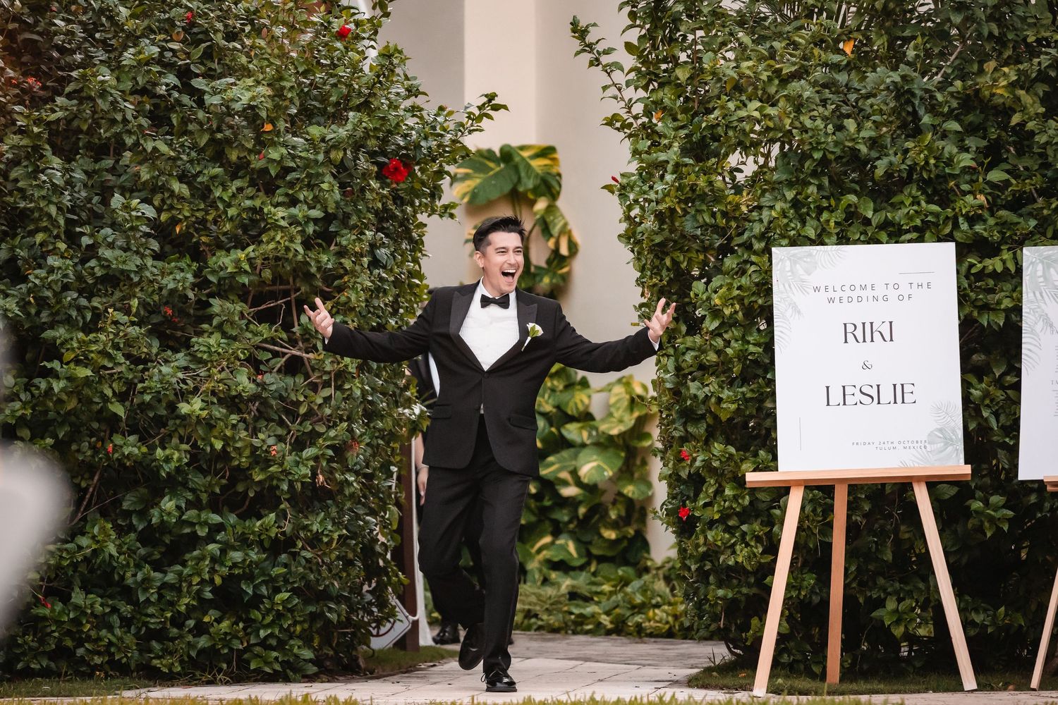 Wedding reception seating chart displayed on elegant white stands with greenery backdrop.