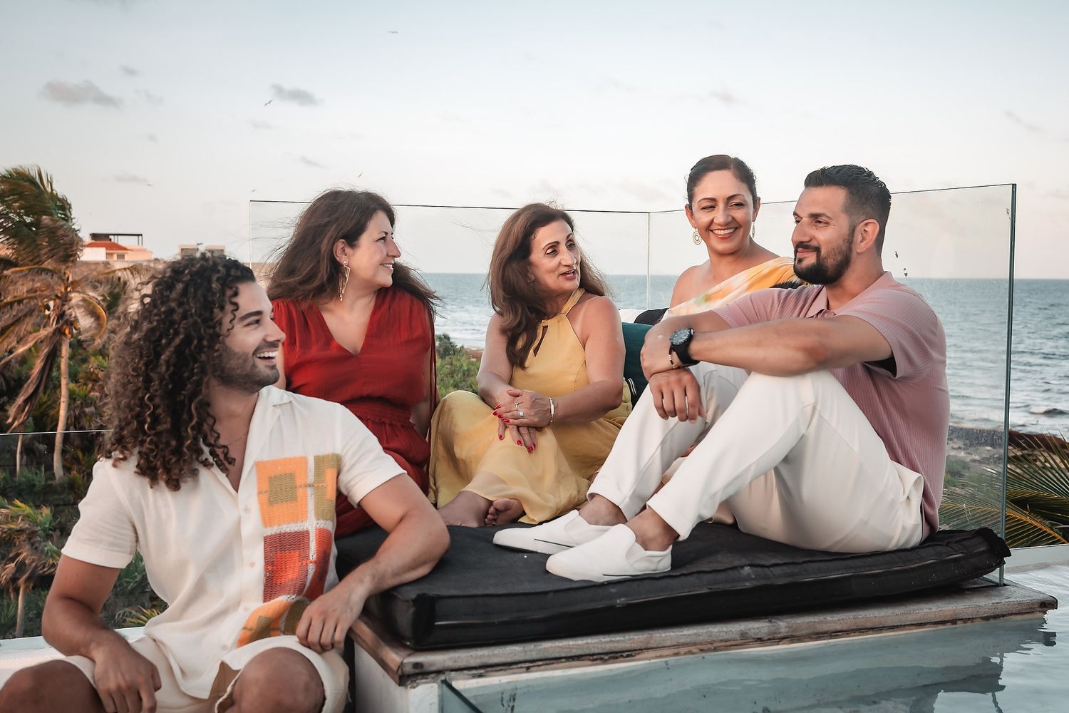 Friends sharing laughs while sitting on a concrete wall overlooking the ocean at sunset.