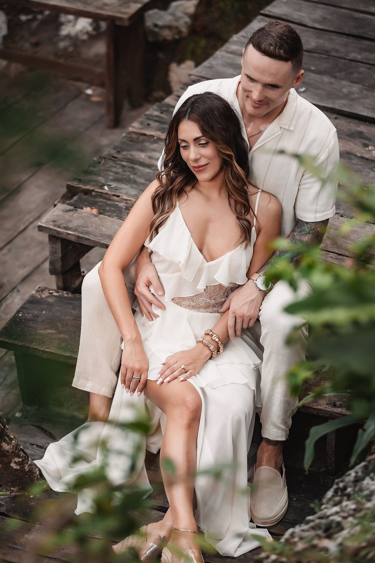 Intimate moment captured on wooden deck with white outfits and natural backdrop.