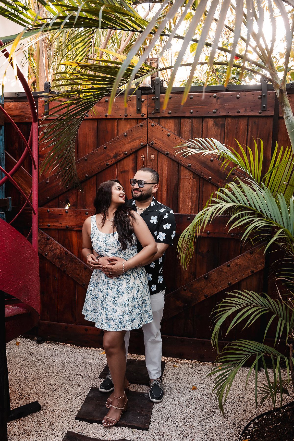 A romantic proposal scene against a wooden fence with palm fronds.