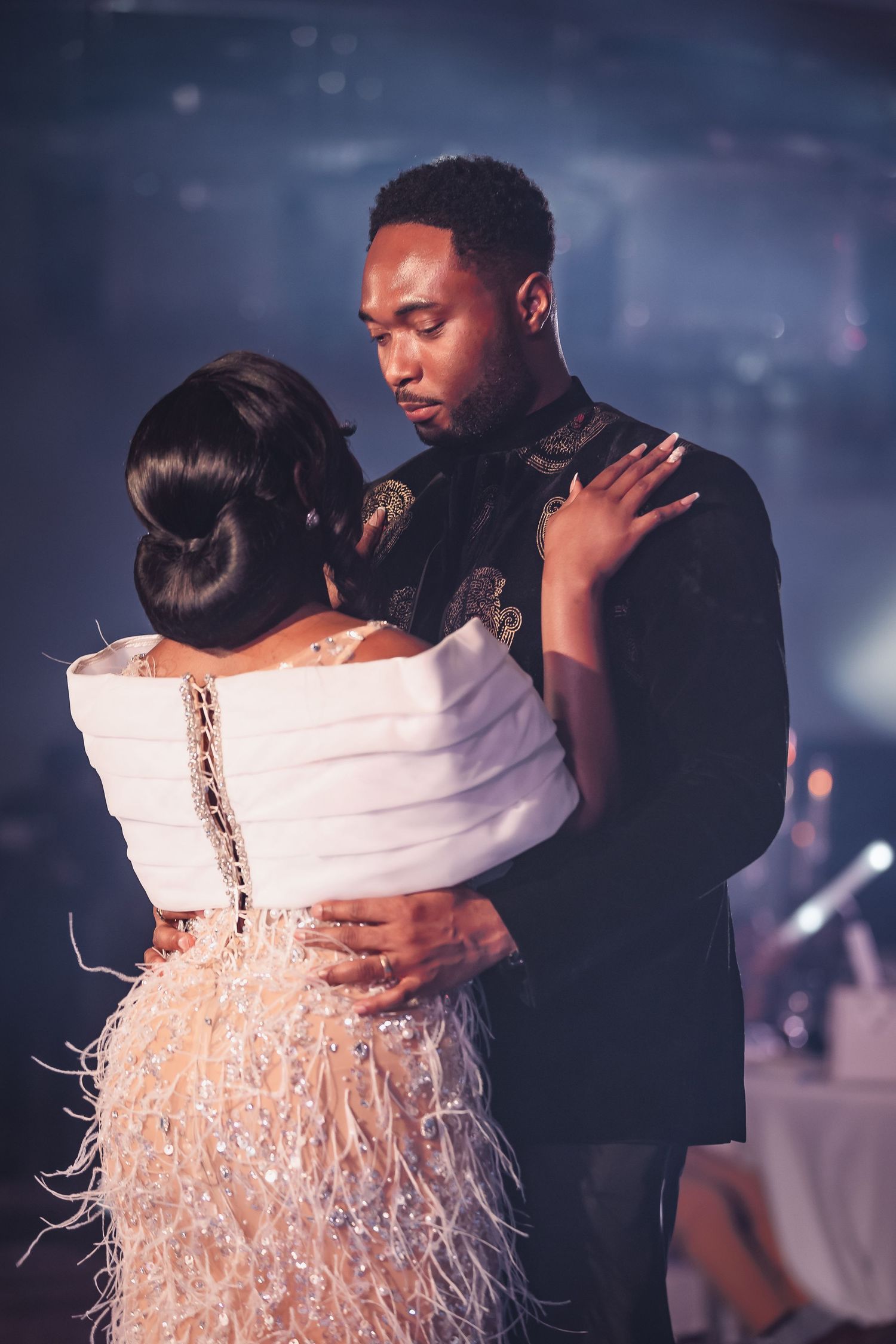 Intimate first dance moment captured with dramatic lighting and feathered dress details.