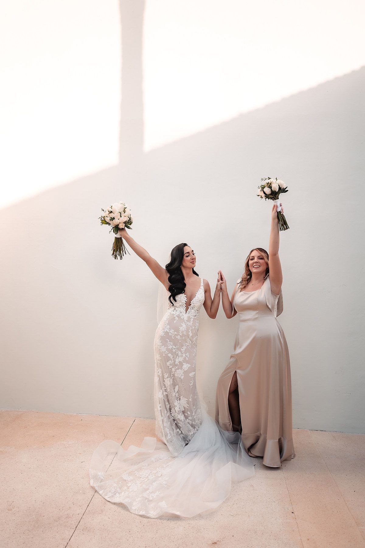 Two wedding dresses displayed in a bright white studio with joyful poses and bouquets.