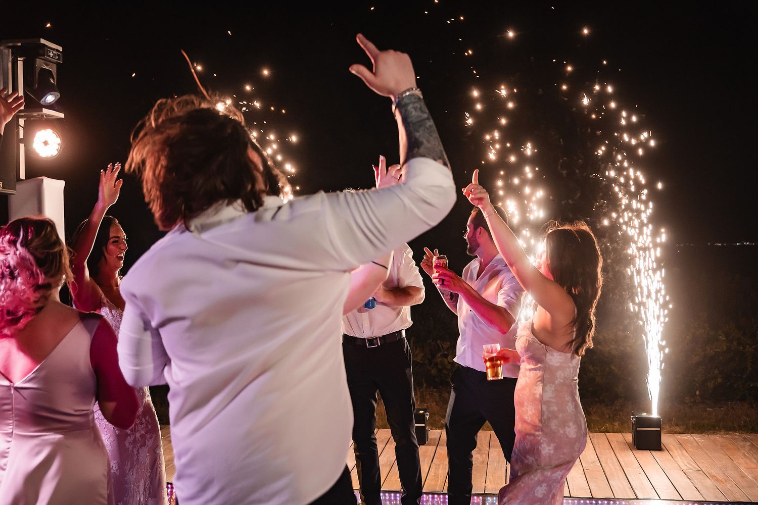 Wedding party dancing under sparklers at night celebration.
