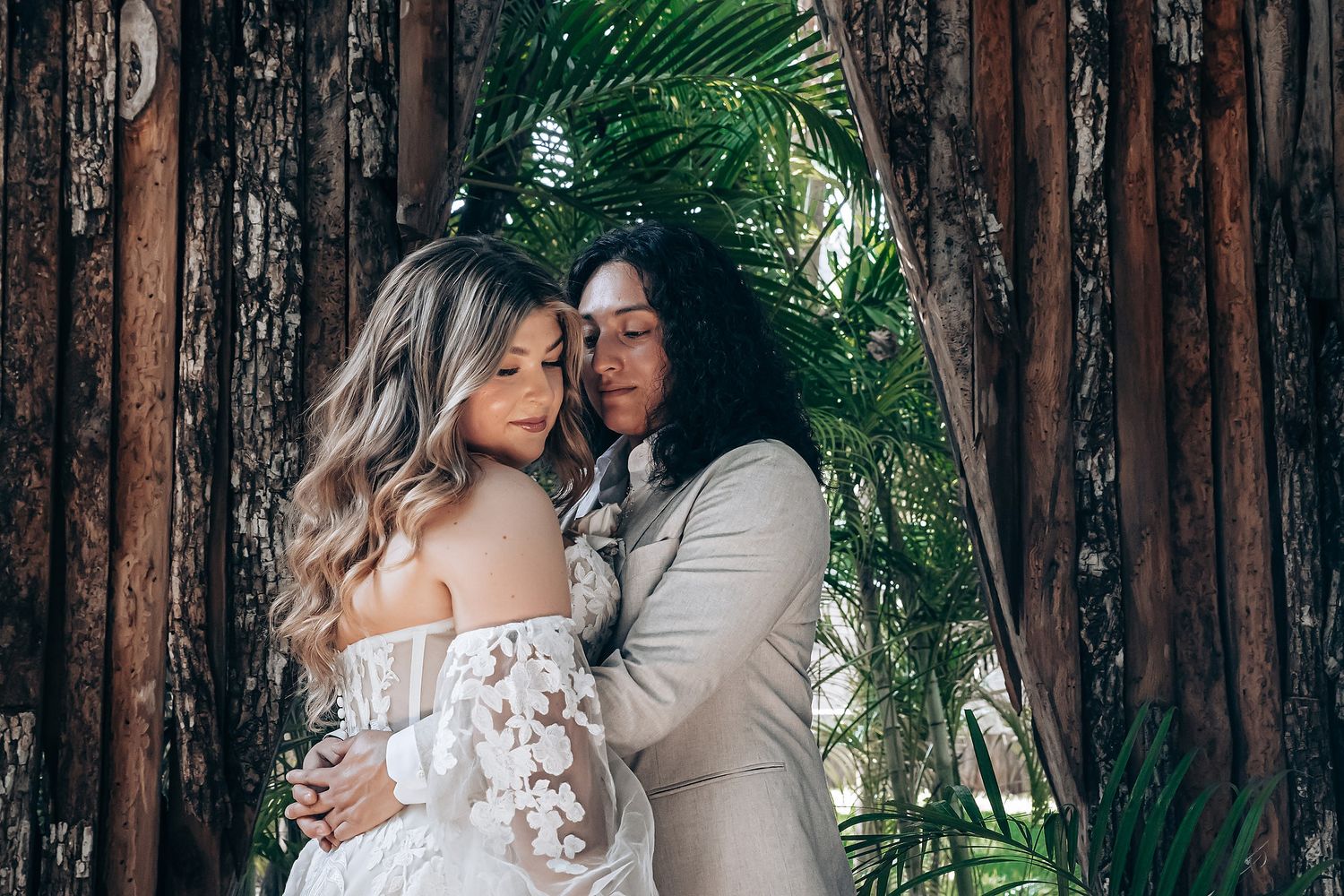 Romantic wedding couple embracing in front of wooden wall with tropical greenery.
