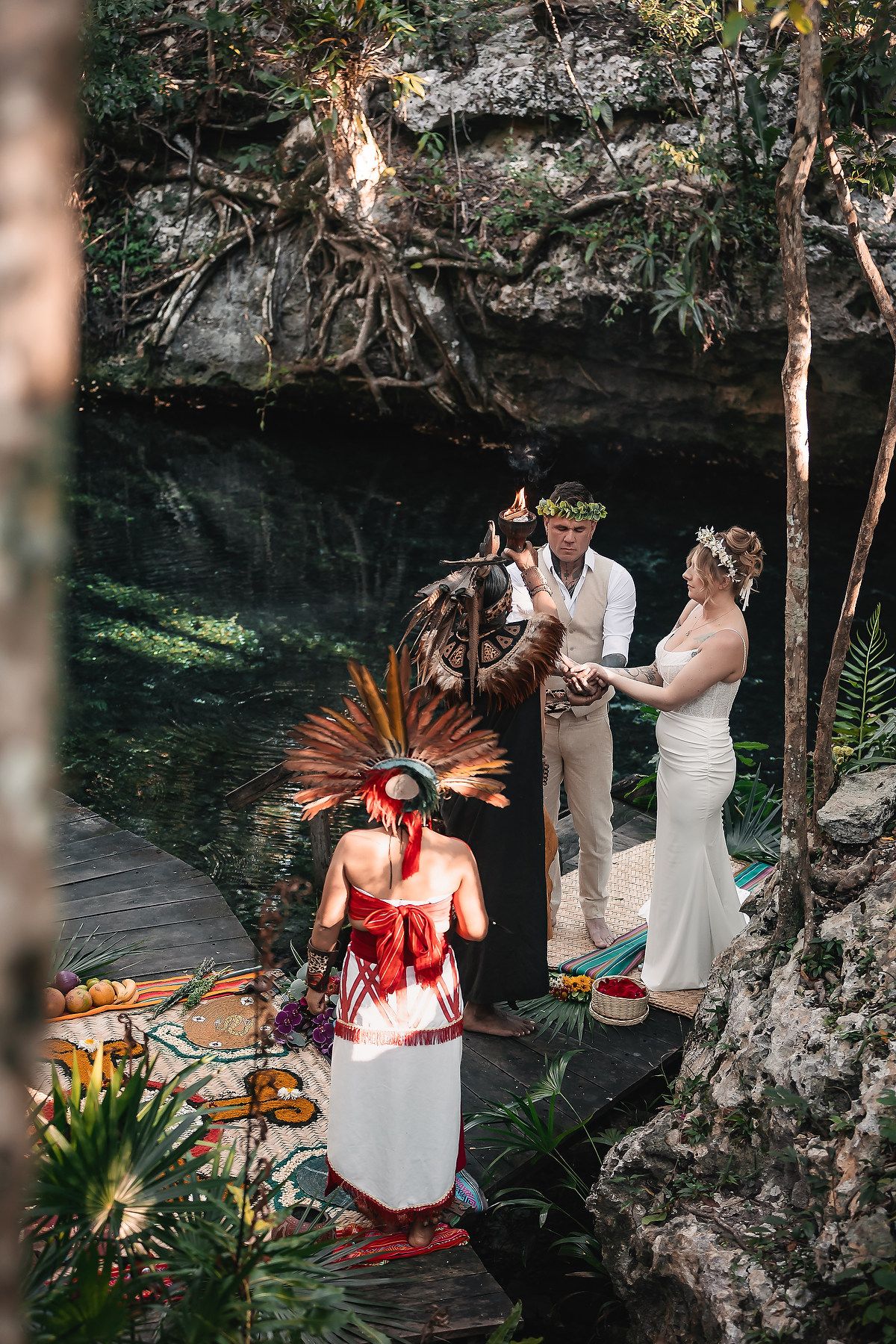 A traditional ceremony takes place at a scenic cenote in Mexico with tropical plants and rocky formations surrounding the water.