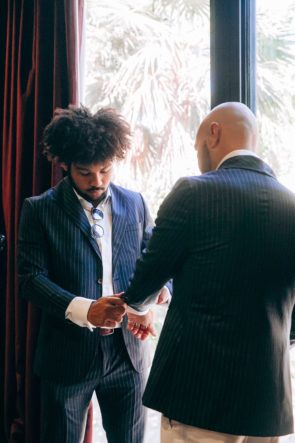 A sequence of four photos showing two people in pinstripe suits having a conversation in front of dark curtains.