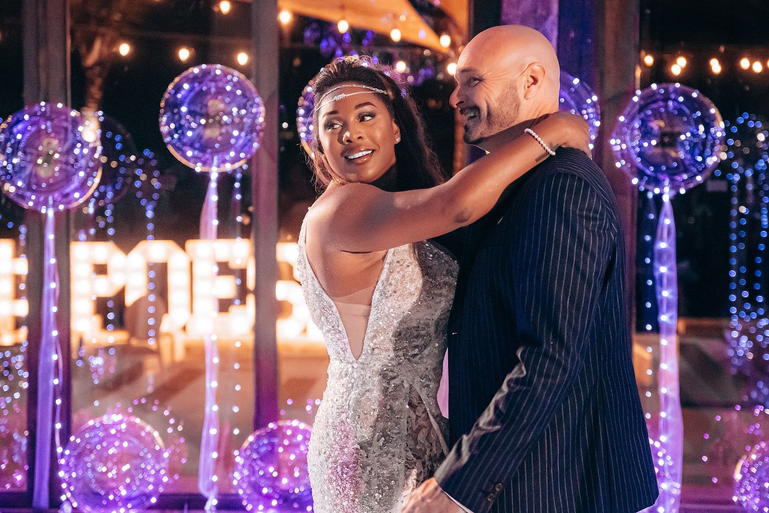 Newlyweds dance under glowing LED balloons at an elegant evening reception with purple lighting effects.