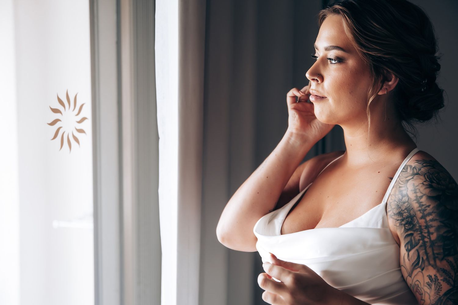 Close-up view of a person getting ready with elegant bridal makeup and hair in a white top with visible tattoos.