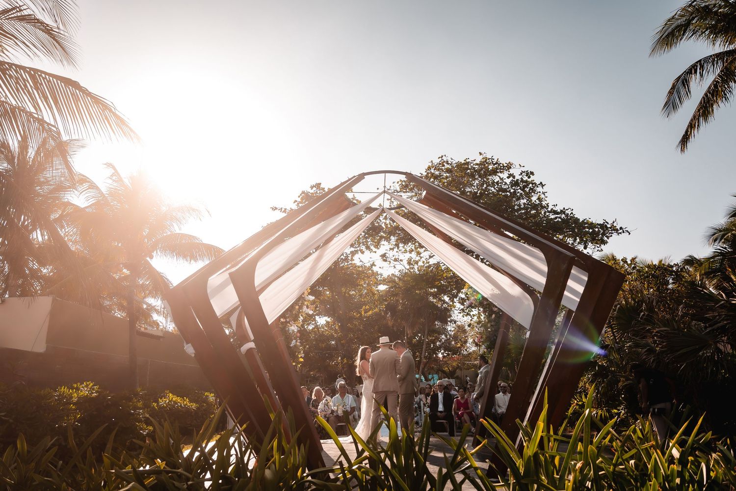 Palm trees and wedding decorations silhouetted against a bright sunset sky.