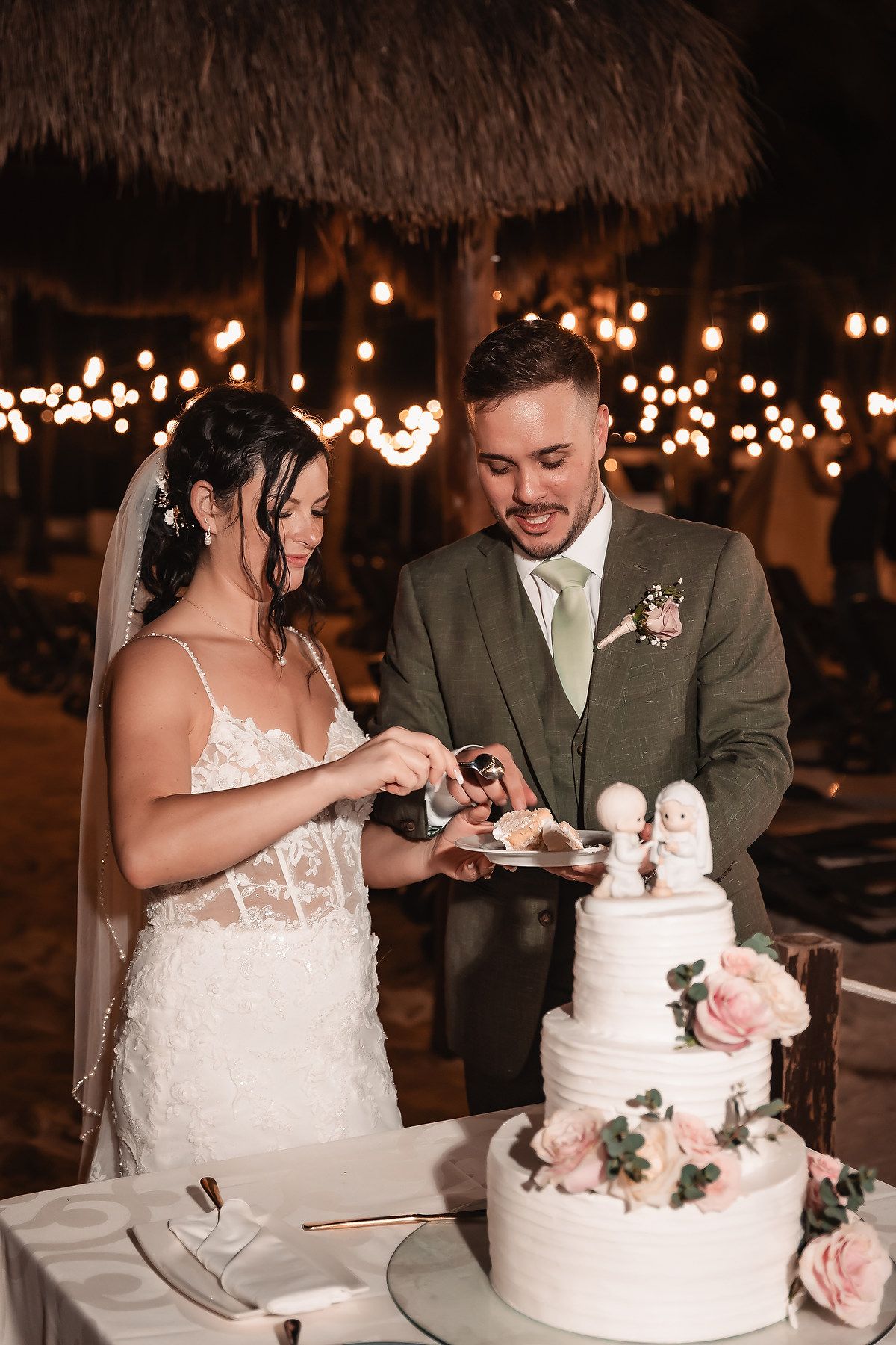 Wedding couple cuts their elegant white tiered cake decorated with pink roses.