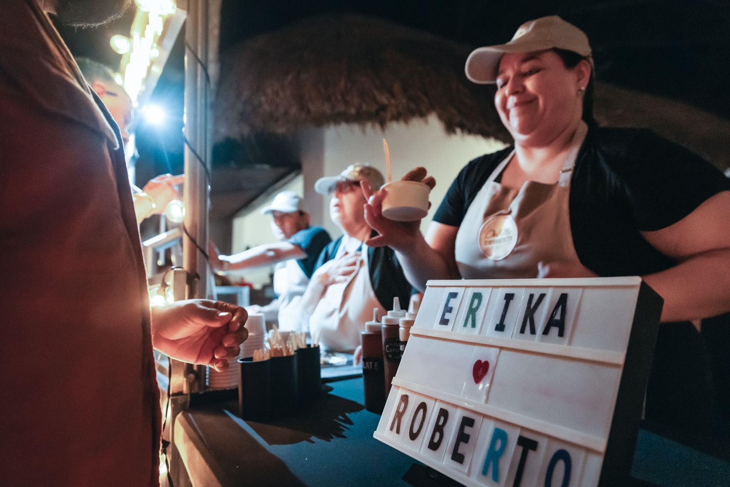 Wedding staff serving guests at Erika and Roberto's reception celebration with a decorative light-up sign display.