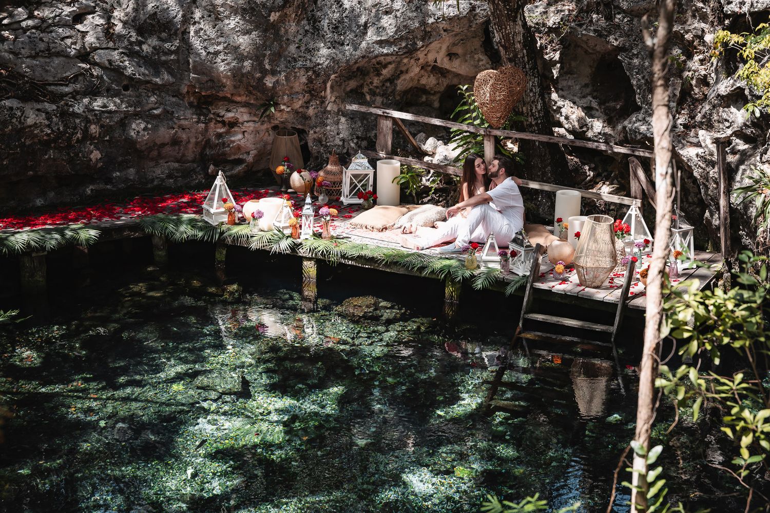 Woman relaxing on an elegantly decorated wooden platform over a serene cenote in a jungle cave.