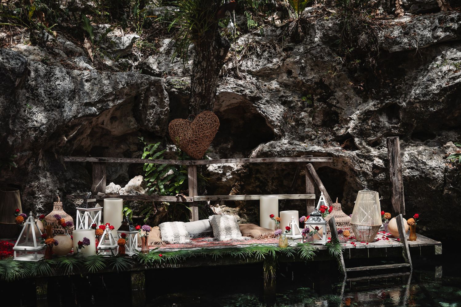 Rustic outdoor wedding dessert table set against a rocky cave backdrop with candles and heart decor.