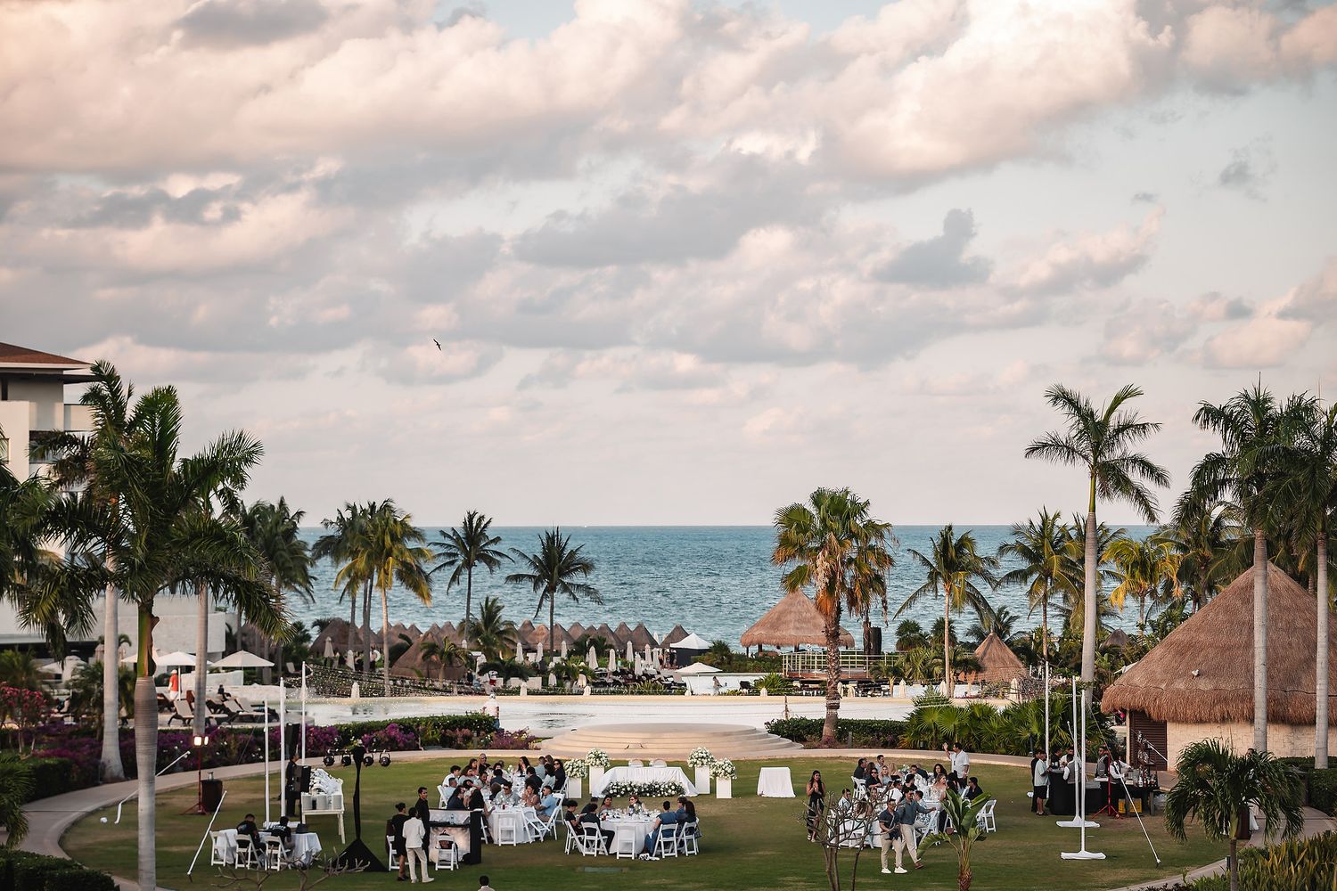 Outdoor beachfront wedding reception with palm trees, white tables, and ocean views at a tropical resort.