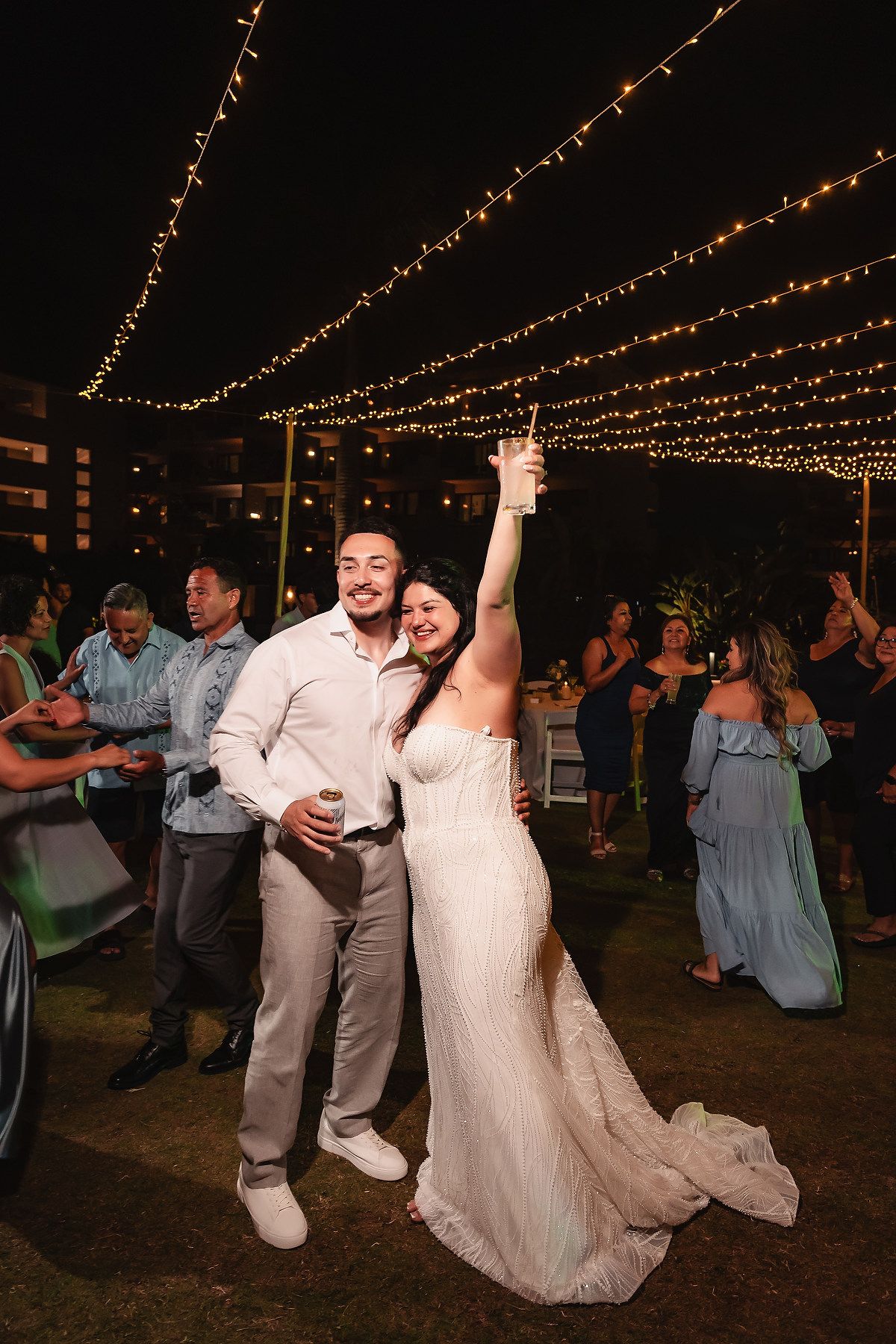 Bride and groom celebrating at outdoor wedding reception under string lights at night.