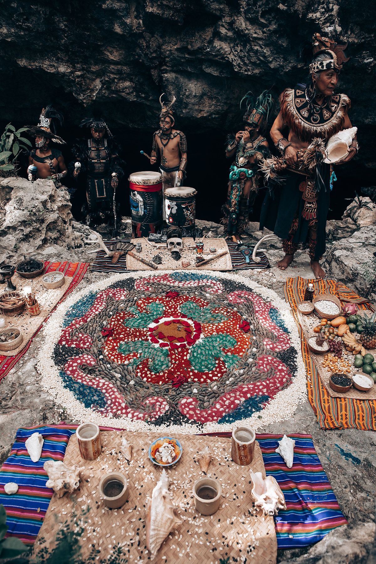Colorful Mayan ceremonial mandala altar with performers in traditional costumes inside a cave.