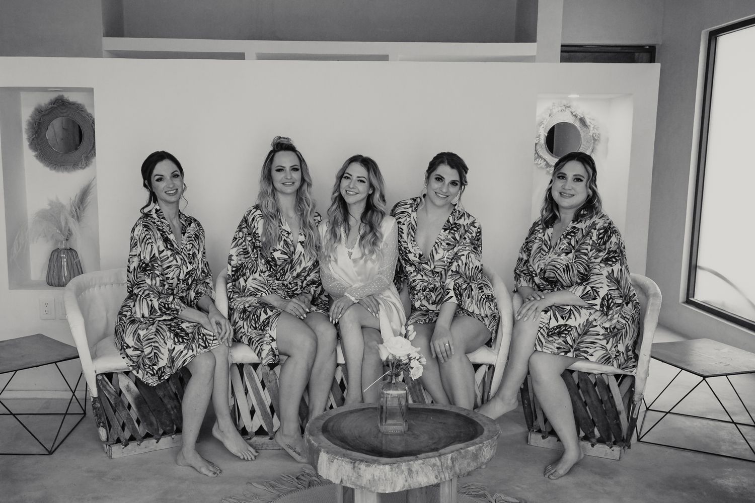 Black and white photo of a bride and four bridesmaids in floral robes sitting together during wedding preparations.