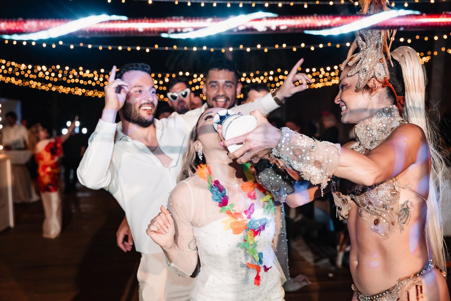 Bride and groom celebrate with colorful leis and performers at festive wedding reception.