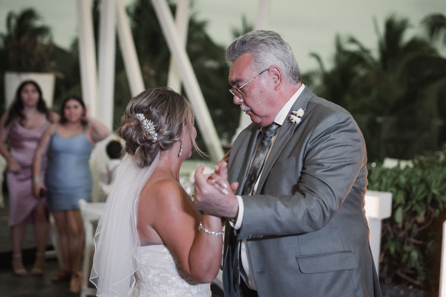 Emotional father daughter dance moment at wedding reception with guests watching in background.