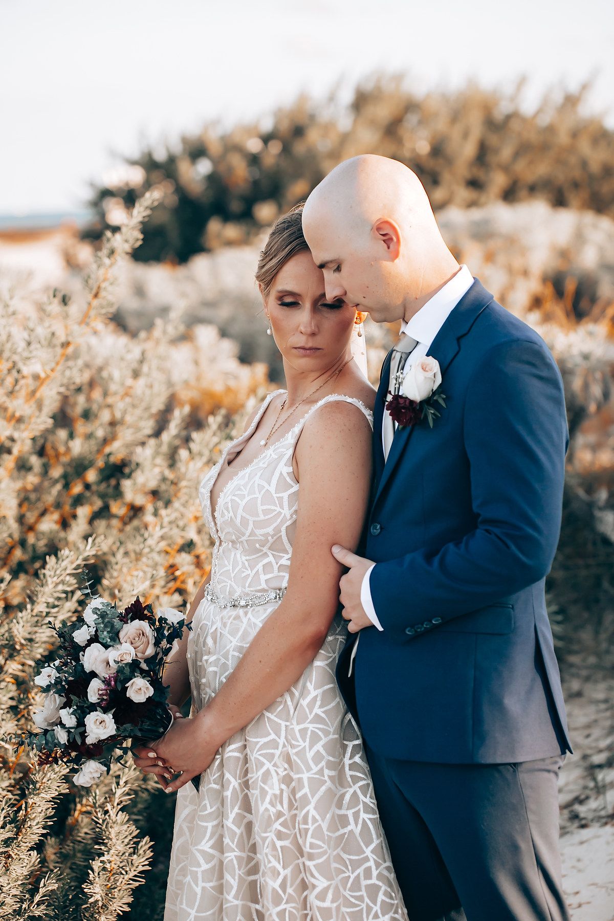 A bride and groom embracing and gazing at each other in a scenic outdoor setting.