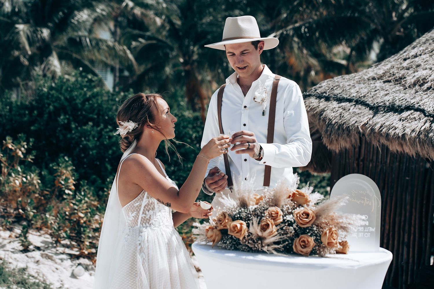 A romantic beach wedding scene with white decor and tropical palm trees.
