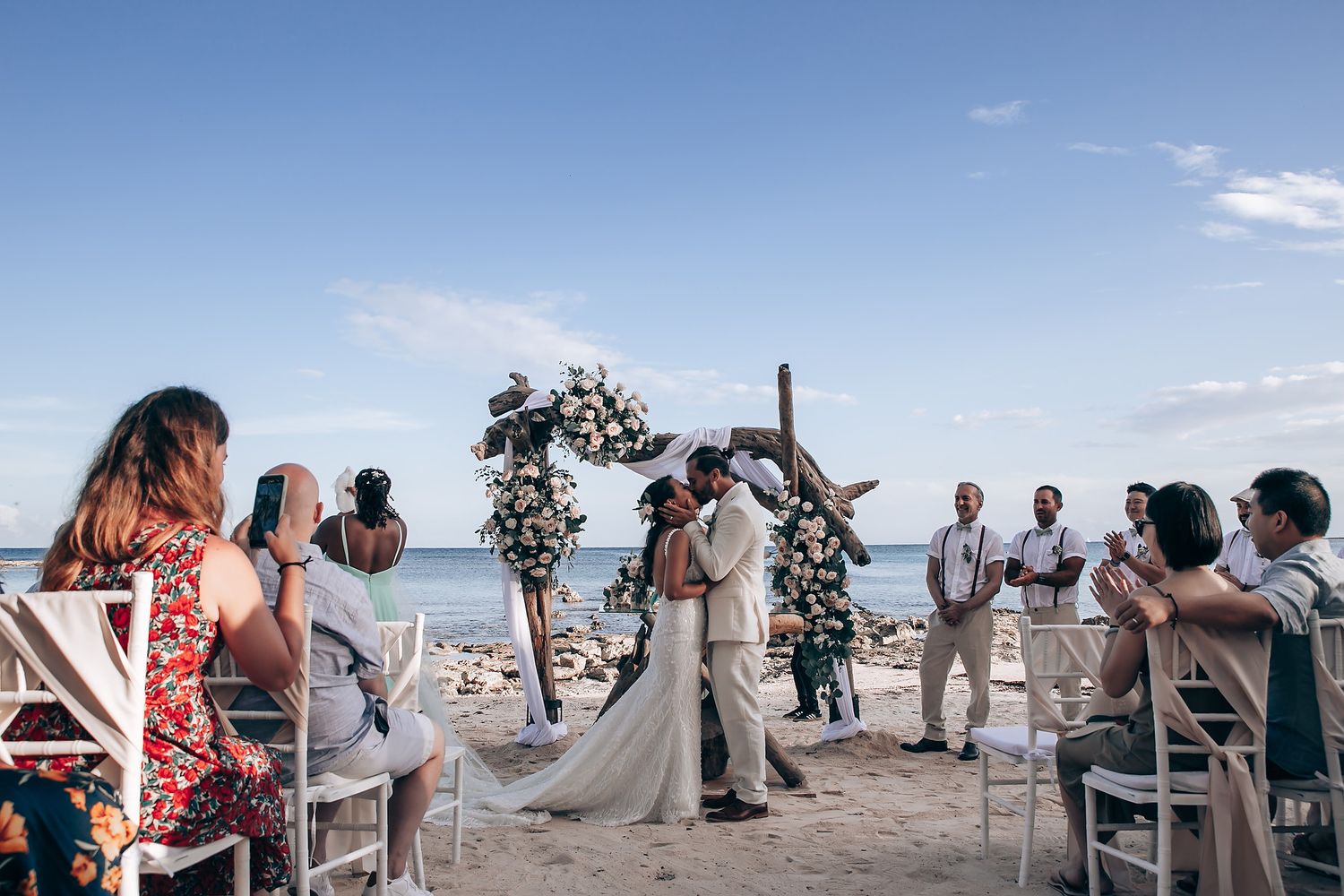 A beachfront wedding ceremony setup with white chairs and floral arrangements against an ocean backdrop.