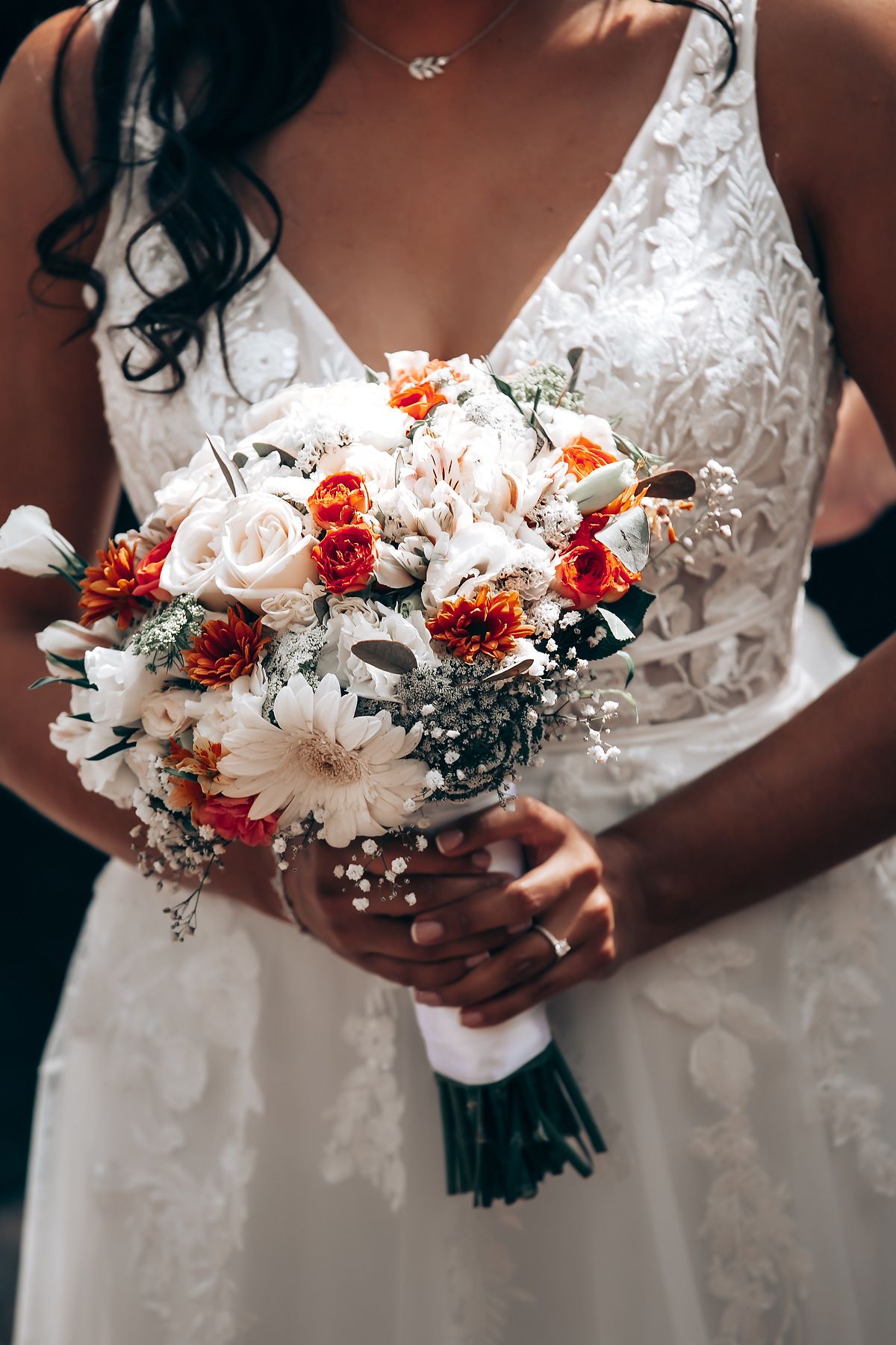 Close-up shots of a bridal bouquet featuring white daisies, orange flowers and delicate foliage against a white dress.