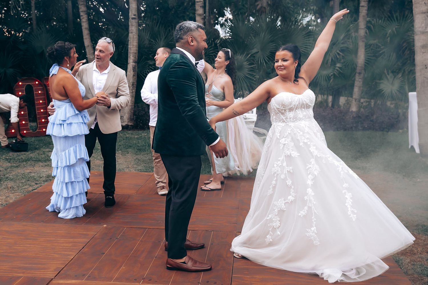 Wedding celebration on an outdoor wooden dance floor with guests dancing.