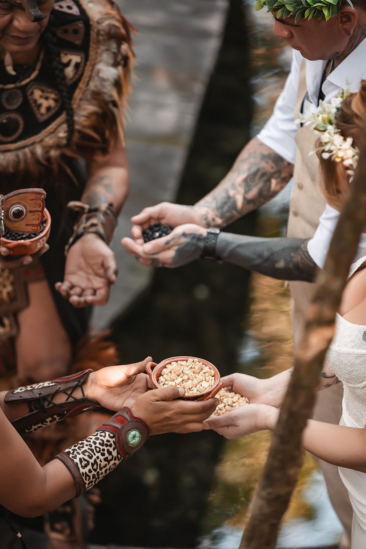 Tattooed groom and bride receiving ceremonial seeds during a traditional outdoor wedding ritual.