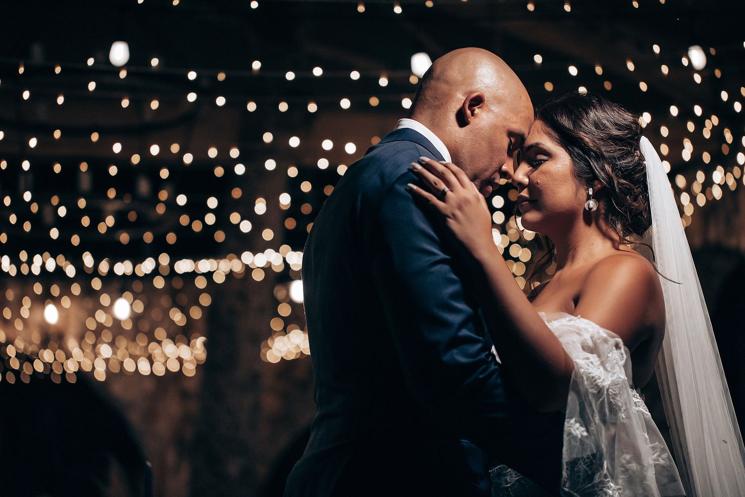 A romantic wedding couple shares intimate kisses under twinkling string lights during their reception celebration.