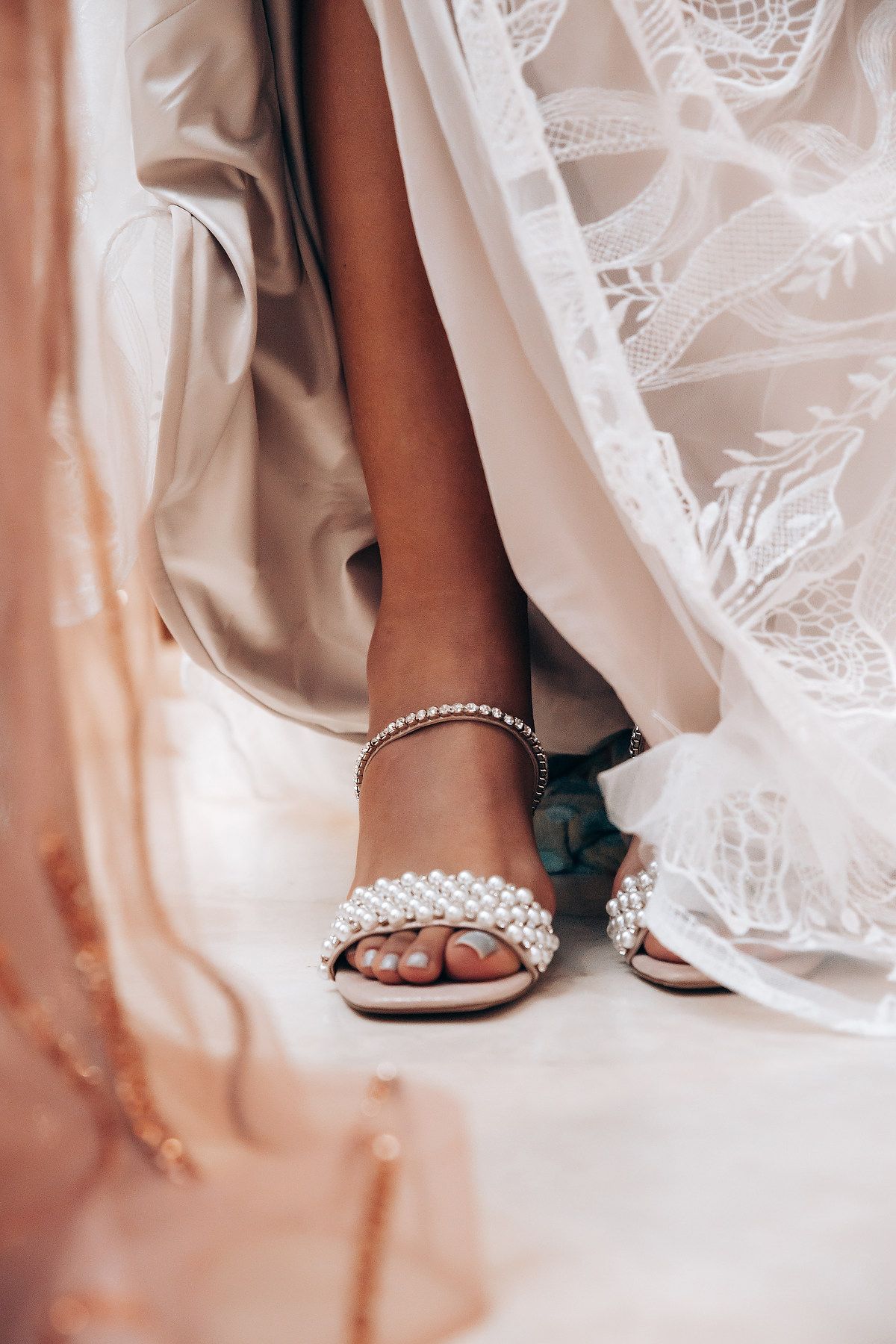 Close-up details of elegant bridal shoes and lace dress hem on a light background.