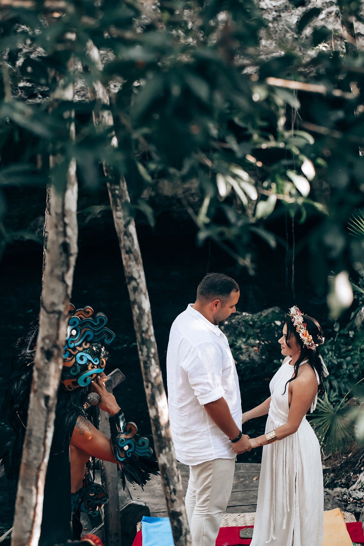 A couple in white attire shares a romantic moment during an outdoor photo session in a wooded setting.