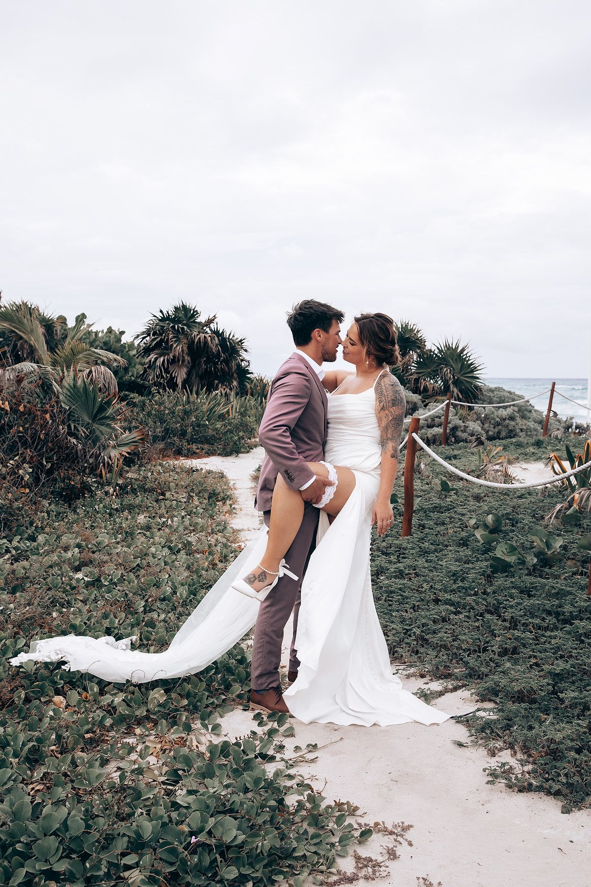 Couple poses for romantic wedding photos on a coastal path with flowing veil.