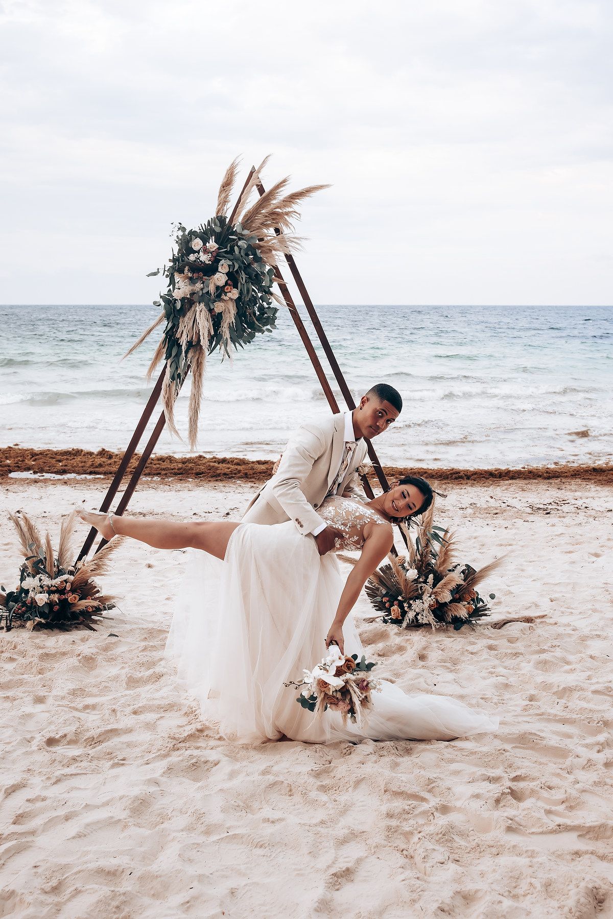 Artistic beach wedding photos with a floral arch and flowing white dress against the ocean.