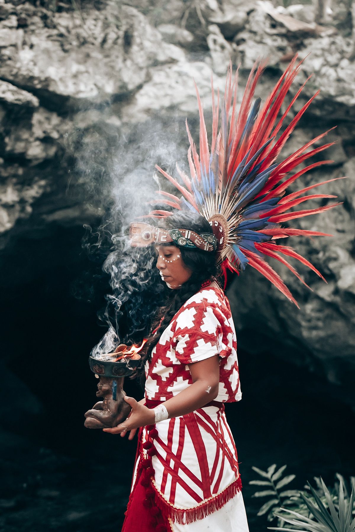 Traditional dancer in red and white regalia with feathered headdress performing a ceremonial dance.