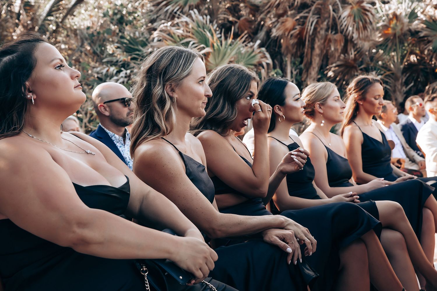 Wedding guests seated in rows of black dresses watching an outdoor ceremony.