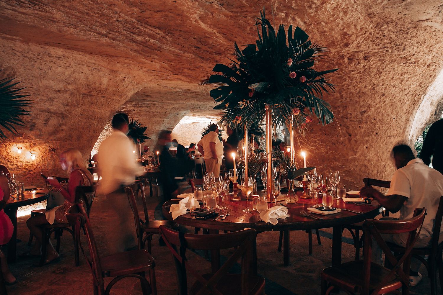 An elegant wedding reception table setting in a cave-like venue with dramatic lighting and palm decor.