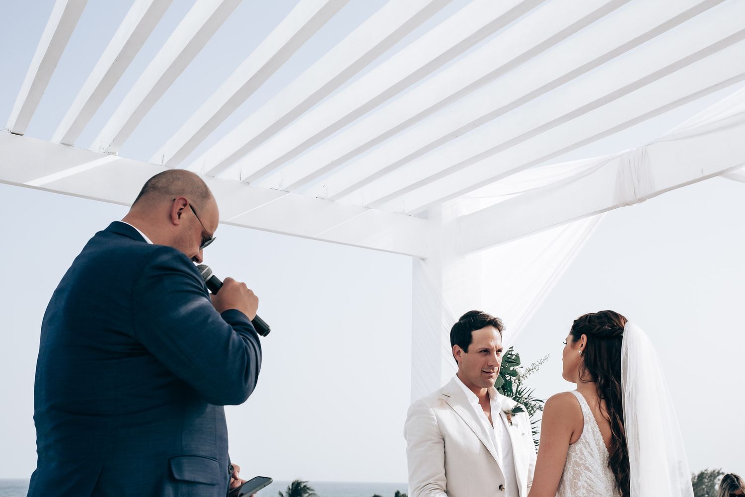 Wedding party members in white attire preparing for the ceremony under a bright pergola.