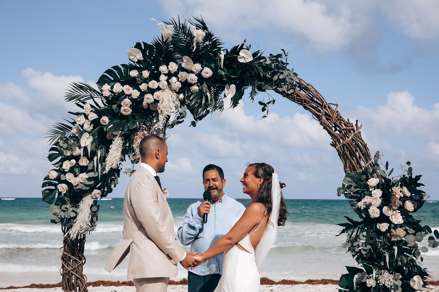 Wedding arch decorated with white flowers and greenery on a beautiful beach with turquoise waters.