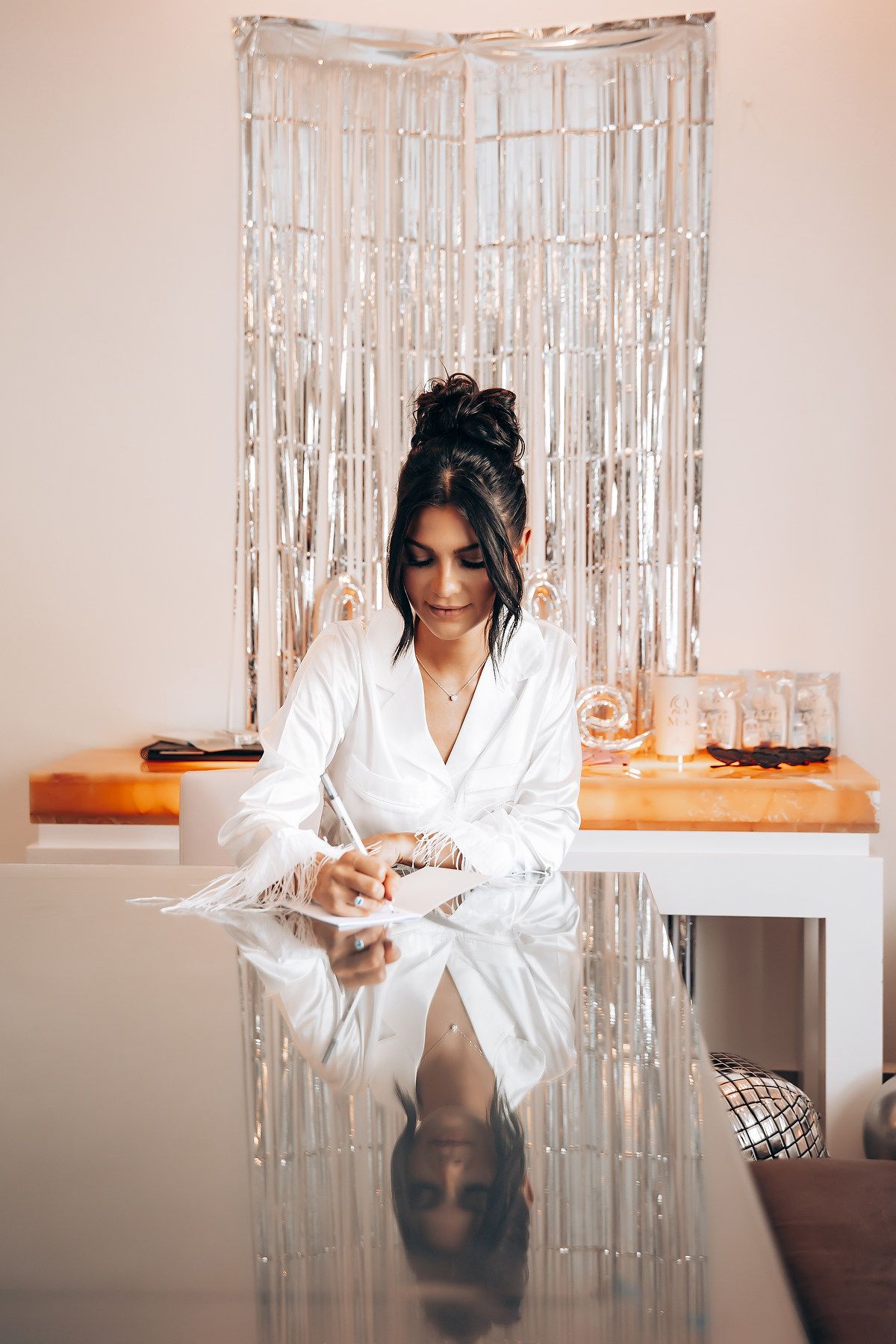 Bride in white robe getting ready with sparkly backdrop and soft lighting.