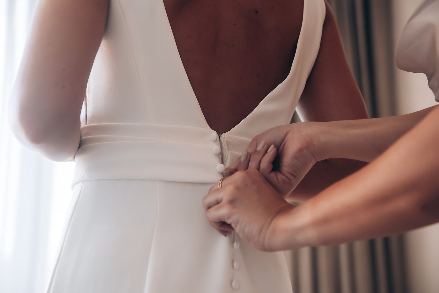 Close-up shot of hands adjusting a white wedding dress with delicate fabric details.