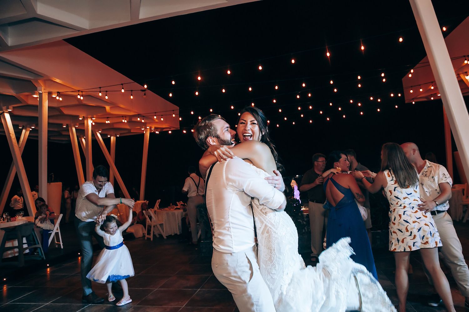 Couples dancing at nighttime wedding reception under string lights.