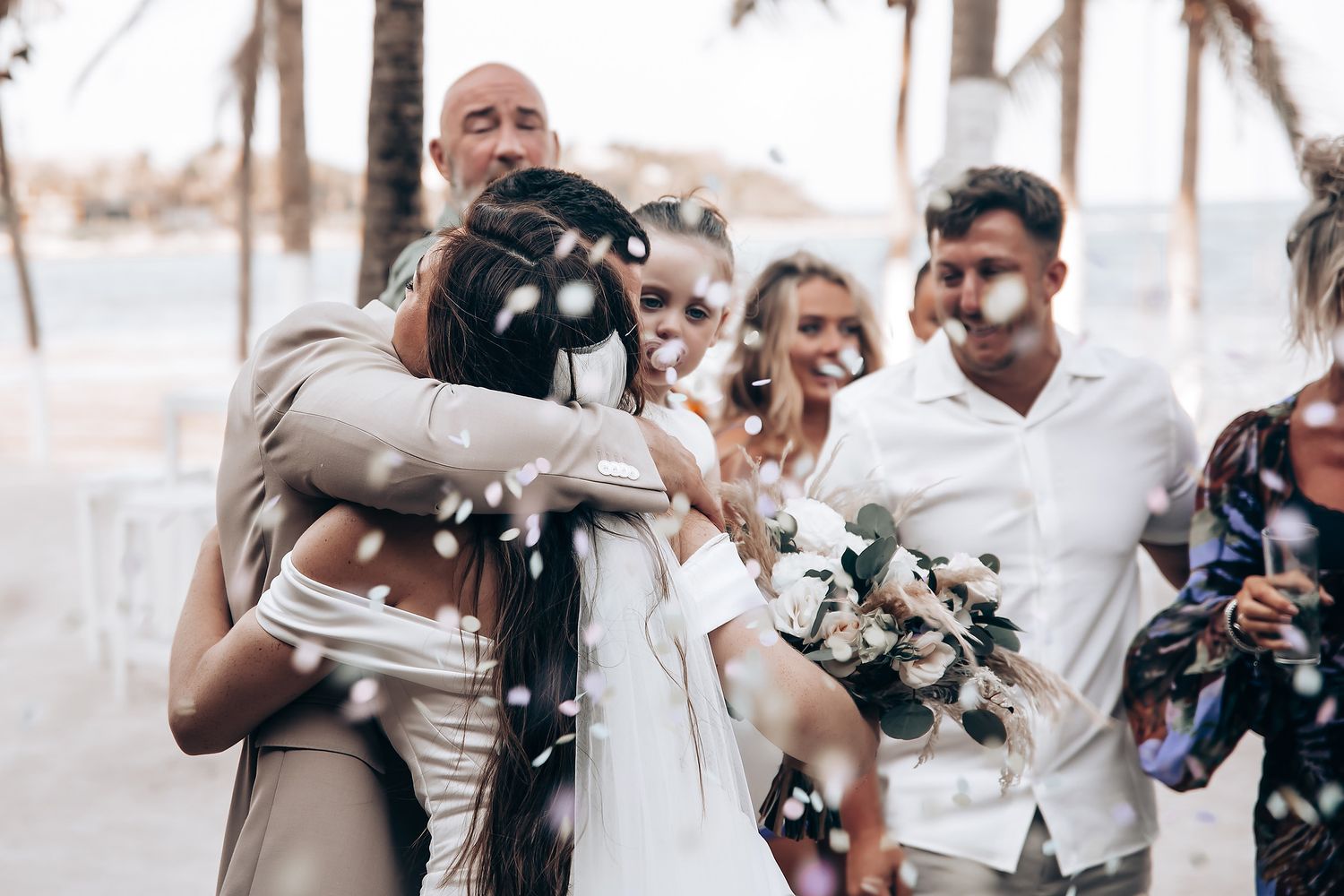 A group of wedding guests popping champagne bottles outdoors on a sunny day.