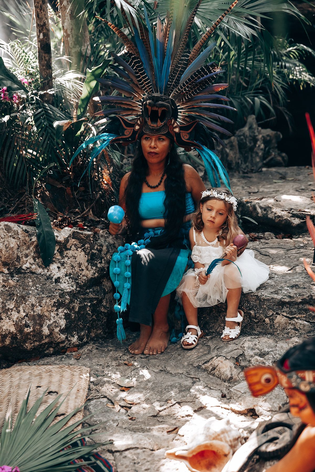 Traditional Mayan ceremonial elements displayed in a tropical garden setting with vibrant feathered headdresses.